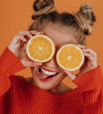 The girl holds in her hands halves of an orange near her eyes