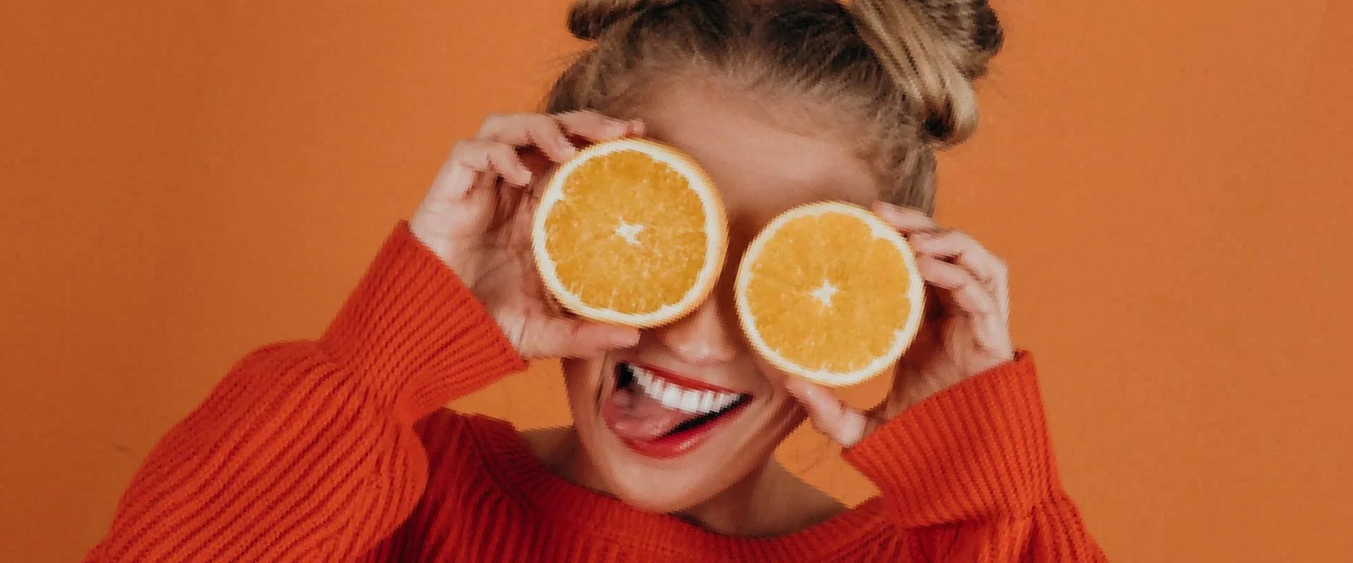 The girl holds in her hands halves of an orange near her eyes