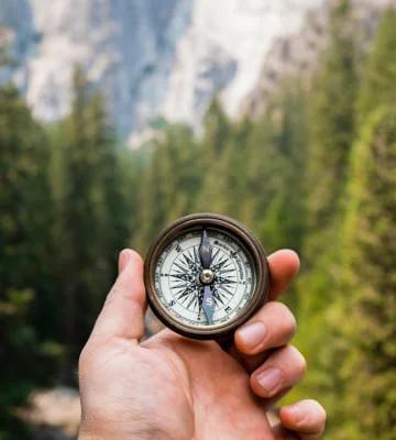 Compass in hand against the background of trees and mountains