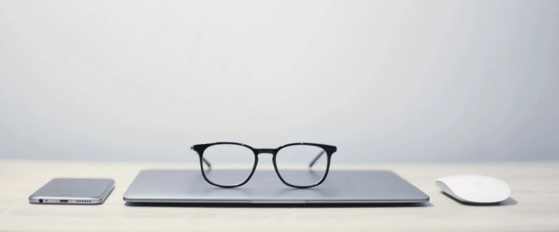 Mobile phone, glasses on laptop and computer mouse on the table